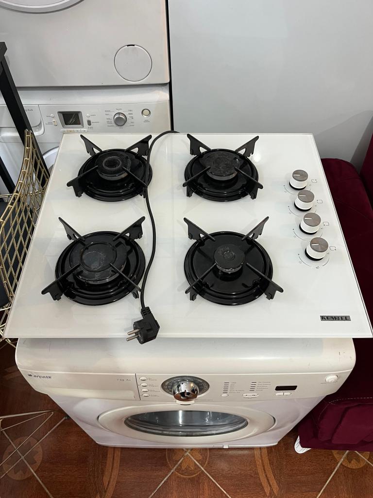 Bir mutfak ocak seti, dört gaz brülörü ve kontrol düğmeleriyle birlikte, altındaki beyaz bir bulaşık makinesiyle birlikte görüntüleniyor.