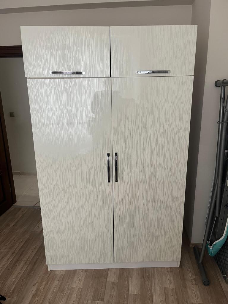 Beyaz renkli, kapaklı bir dolap, iç düzenlemesi için geniş bir alan sunuyor.